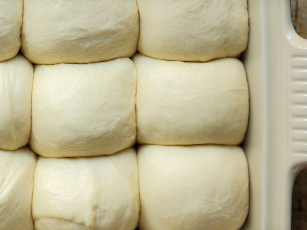 Close-up of uncooked, fluffy dough rolls neatly arranged in a baking dish, ready for baking.